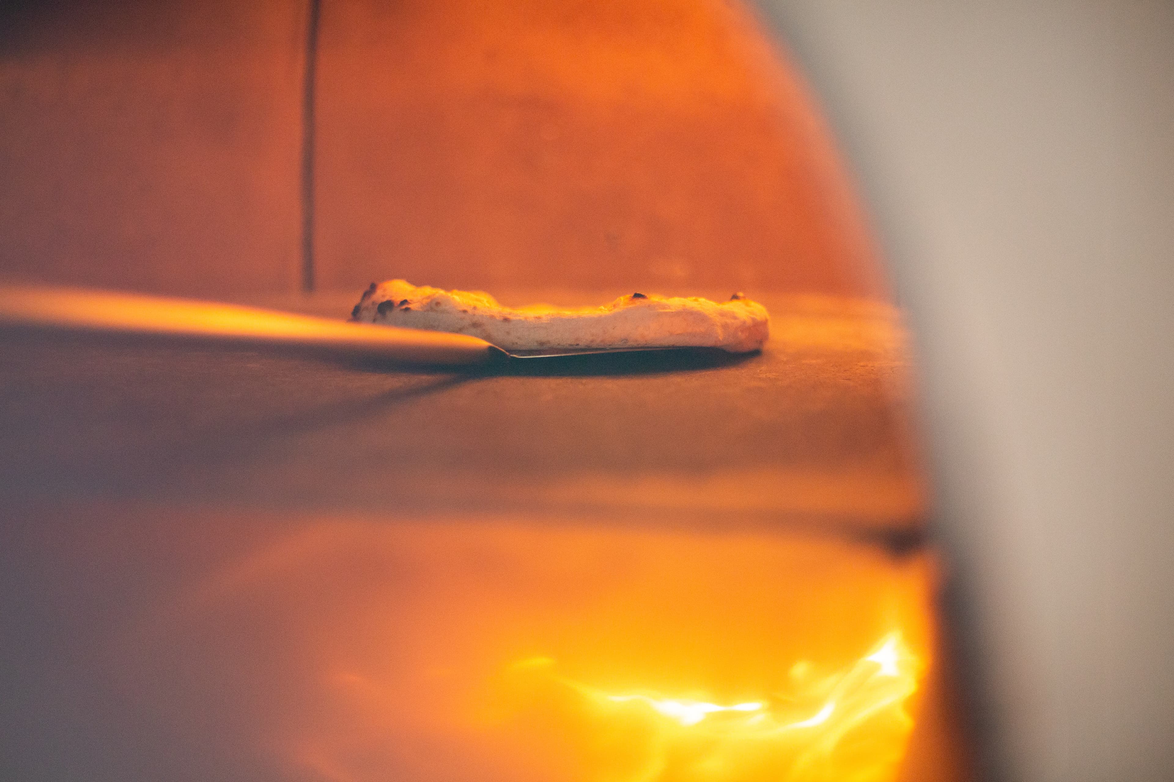 Pizza en cuisson dans un four professionnel — vue rasante sole et flammes